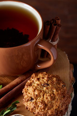 Christmas concept with a cup of hot tea, cookies and decorations on a log over wooden background, selective focus