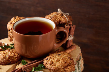 Christmas concept with a cup of hot tea, cookies and decorations on a log over wooden background, selective focus