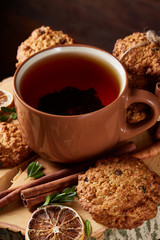 Christmas concept with a cup of hot tea, cookies and decorations on a log over wooden background, selective focus