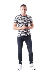 Naklejka premium Handsome muscular stylish man in camo shirt holding mobile phone and looking at camera. Full body isolated on white background. 