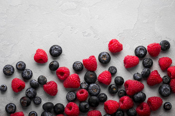 Fresh blueberries and raspberries on light concrete background, overhead view, copy space