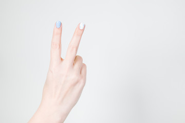 Closeup view of white female hand in victory gesture isolated on white background. Fingernails with modern gel polish manicure of white and blue colors.