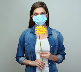 Young woman wearing medical mask holding yellow flower.