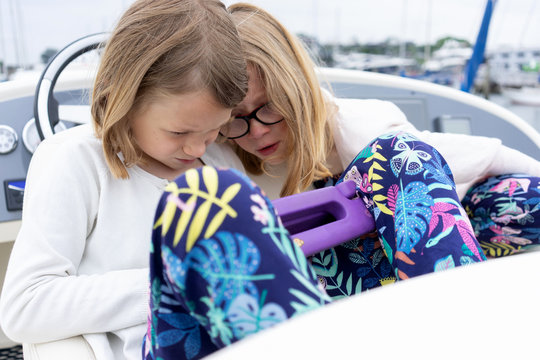 Two Sisters Sitting At The Helm Of A Boat On A Tablet