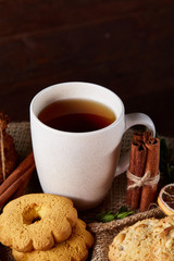 Traditional Christmas tea concept with a cup of hot tea, cookies and decorations on a wooden background, selective focus