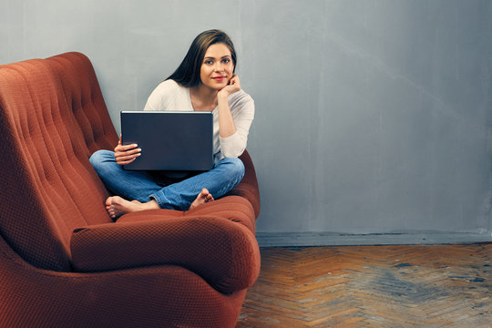 smiling young woman casual dressed sitting on sofa with laptop.