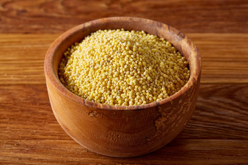 A wooden dish with millet on rustic wooden background, top view, close-up, selective focus.
