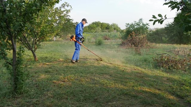 Man walks with lawn mower and mows grass at sunny summer day