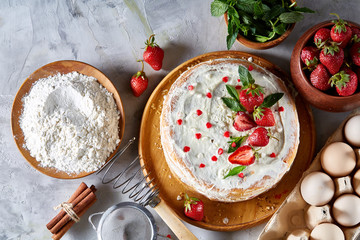 Strawberry tart covered with whipped sour cream surrounded by organic ingredients over white background, flat lay.