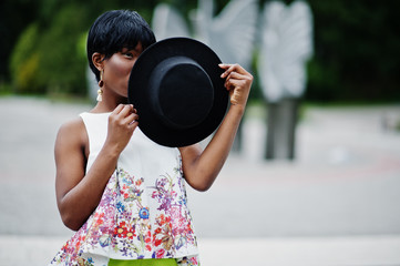 Amazing african american model woman in green pants and black hat posed at park.