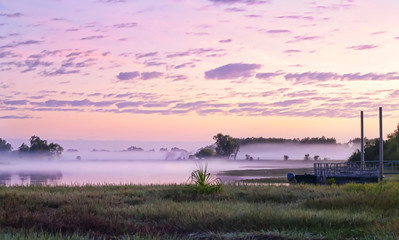 Sunrise over a pier in the Yellow Water billabong in the Kakadu National Park, Australia. Dusk on a river in nothern Australia with beautiful pink sky and clouds © Alex