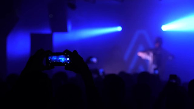Mobile phones shooting a music concert by spectators silhouettes in a stage lights