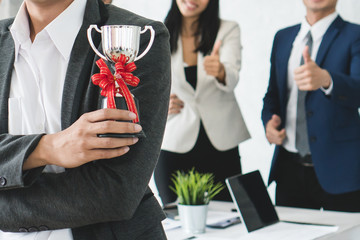 Worker holding trophy prize for best employees of the month in his hand. People in team celebrating...