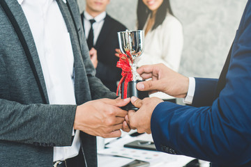 Worker holding trophy prize for best employees of the month in his hand. People in team celebrating...