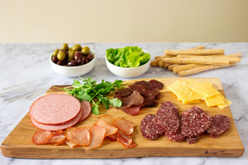 Appetizer table for wine or beer with sausages, dried meat and cheese, served with grissini, herbs and olives.
