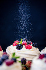 Homemade meringue basis for cake Pavlova with fresh blueberries and BlackBerry and powdered sugar on black concrete texture background. Copy space