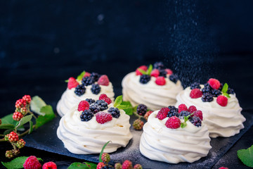 Homemade meringue basis for cake Pavlova with fresh blueberries and BlackBerry and powdered sugar on black concrete texture background. Copy space