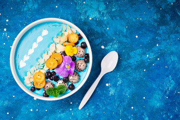 Blue smoothie bowl with fruits, berries, nuts and flowers. Tropical healthy smoothie dessert. Healthy food, vegetarian, diet concept. Top view. Copy space