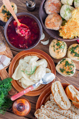 Traditional food in the Ukrainian cuisine - borsch, vareniki, bacon, broth, nalgovniki, cutlets in Kiev, dranniki, pampushki, on a wooden table, selective focus, top view