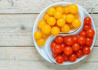 Yellow and red cherry tomatoes with water drops. Fresh and juicy organic vegetables in a white plate on a wooden table