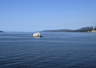 view across the ocean towards a ferry with the Powell River pulp mill and coastline in the background, British Columbia Canada