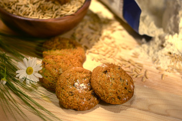 Still life with oatmeal cookies, spikelets of wheat, oat grains and a pack of flour on a wooden table.