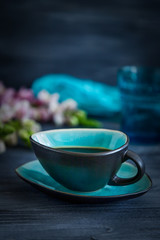 Black coffee in a turquoise cup and flowers on a black background. Low key, free space