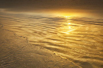 Beautiful golden reflection of the sunset on the sand beach with soft wave.