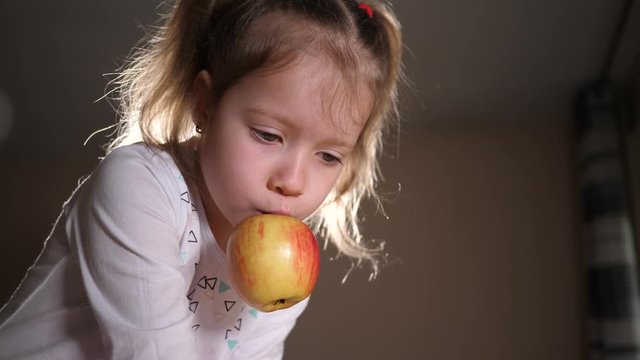 Little funny child girl at home play and eat organic fruit ripe apple on the table