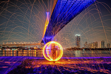 Hot Golden Sparks Flying from Man Spinning Burning Steel Wool under Bhumibol Bridge in Bangkok...
