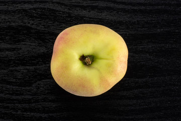 One fresh ripe Saturn peach flatlay on black wood background.
