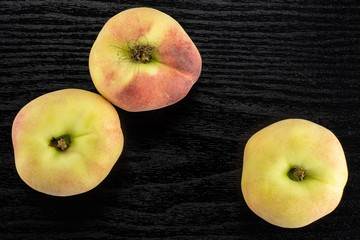 Three fresh ripe Saturn peaches top view on black wood background.