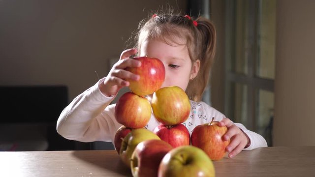 Little cute child girl at home funny play construct with organic fruits ripe apples at the table