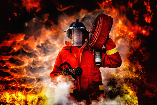 fireman wearing firefighter suit holding a fire hose and nozzle to using water and extinguisher to fighting with fire flame in an emergency situation., burning building in background.