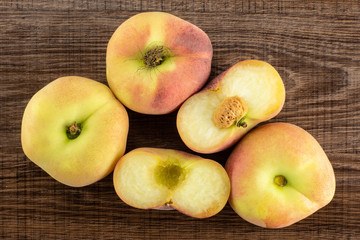 Three fresh ripe Saturn peaches and one cut in two halves top view on brown wood background.