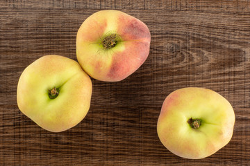 Three fresh ripe Saturn peaches top view on brown wood background.