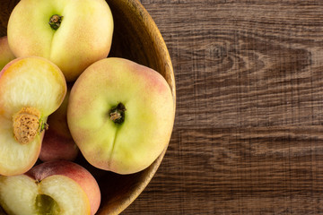Fresh ripe Saturn peaches in a wooden bowl top view on brown wood background.