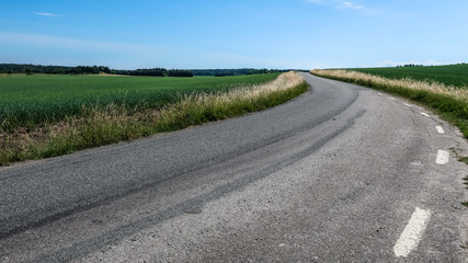 A curvy small road in the Swedish countryside. Open landscape and blue sky.
