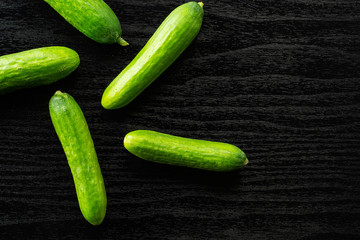 Five fresh mini cucumbers flatlay on black wood background.
