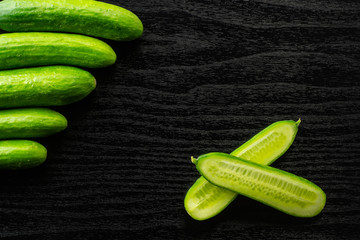 Five fresh mini cucumbers and one cut in two halves flatlay on black wood background.