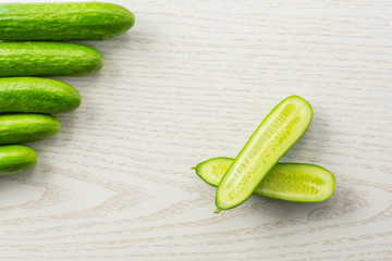 Five fresh mini cucumbers and one cut in two halves flatlay on grey wood background.