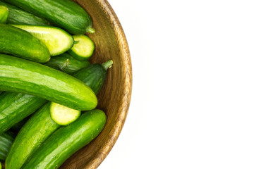 Fresh mini cucumbers in a wooden bowl flatlay isolated on white background.