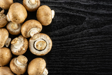 Fresh raw brown champignons top view on black wood background.