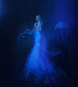 A white mermaid, with very long and blue hair floating under the water. An unusual image, the tail of a jellyfish. Levitation and weightlessness. Pale skin, gentle makeup. Art photo