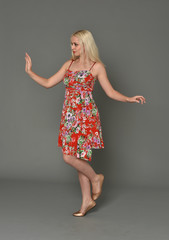 full length portrait of blonde girl wearing red floral dress, standing pose on grey studio...
