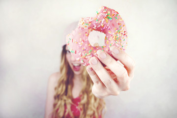 Chica joven sujetando un delicioso donut rosa 