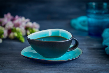 Black coffee in a turquoise cup and flowers on a black background. Low key, free space