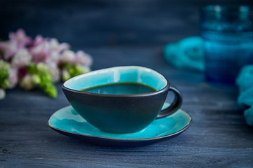 Black coffee in a turquoise cup and flowers on a black background. Low key, free space