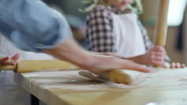 Close up hands of unrecognizable young man rolling out dough on floured surface and showing children how to use rolling pin