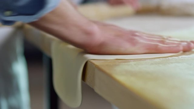 Close up shot of unrecognizable man shaping dough with hands when making pizza on kitchen worktop